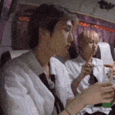 two young men are sitting on a bus eating food and drinking soda .