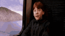a young boy with red hair is looking out a window on a train