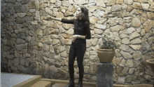 a woman stands in front of a stone wall