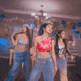 three women are standing in a room with balloons on the wall
