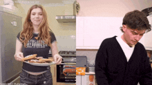 a woman holding a plate of food next to a man who is cooking
