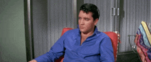 a man in a blue shirt is sitting in a chair with his hands out