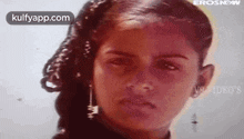 a young girl with curly hair and earrings is looking at the camera .