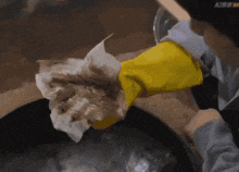 a person wearing yellow gloves wipes a pan with a napkin
