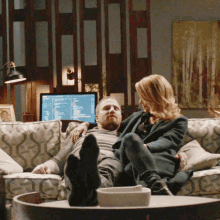 a man and a woman are sitting on a couch with their feet on a table