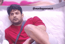 a man in a red shirt is sitting on a white couch with the words @monikagoswamirk above him