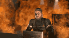 a man is sitting at a desk in front of a computer monitor in front of a fire