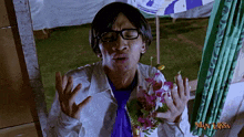 a man with glasses and a purple shirt is holding flowers in front of a man laksa logo