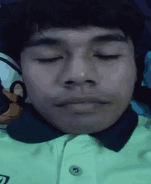 a man with his eyes closed is wearing a green shirt with a black collar .
