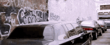 a black car is parked in front of a wall with graffiti on it