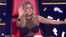 a woman in a black top sits in a red chair waving her hand