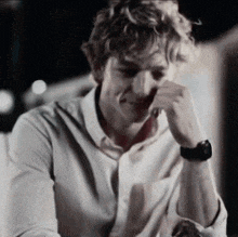 a man wearing a white shirt and a watch is sitting at a table with his hand on his face .