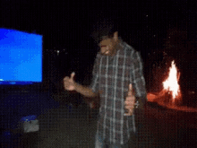 a man in a plaid shirt is standing in front of a fire