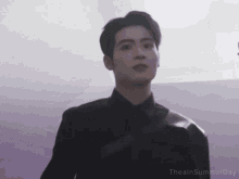 a man in a black suit is standing in front of a purple wall with the words theainsummerday below him .