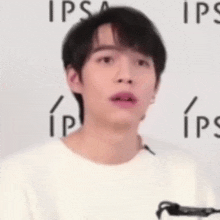 a young man wearing a white t-shirt is standing in front of a wall with ips written on it .