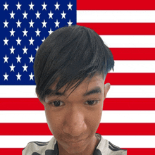 a young man stands in front of a large american flag