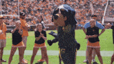 a group of cheerleaders are dancing in front of a mascot wearing a t-shirt