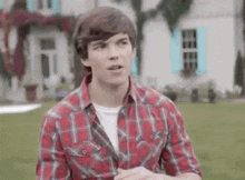 a young man wearing a plaid shirt is standing in front of a house .