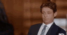 a man in a suit and tie is making a funny face and looking at the camera .