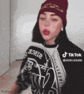 a woman wearing a beanie and a sweater is standing in front of a wall .
