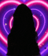 a silhouette of a person standing in front of a heart shaped neon background .