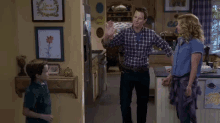 a man in a plaid shirt is dancing in a kitchen with a woman and child .