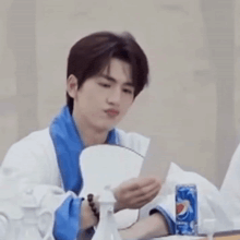 a young man is sitting at a table reading a piece of paper next to a pepsi can .