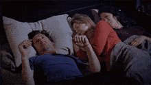 a man and two women are sleeping next to each other in a bed holding hands .