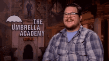 a man is smiling in front of a sign that says the umbrella academy netflix