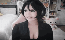 a woman wearing headphones and a black top is sitting in a room with a stuffed animal .