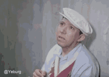 a man wearing a white hat and tie is sitting next to a wall .