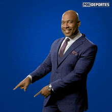 a man in a suit and tie is pointing at something in front of a blue background with fox deportes written on it