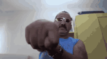 a man wearing sunglasses and a blue tank top has his fist up in the air