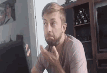 a man with a beard is sitting in front of a laptop computer and making a face .