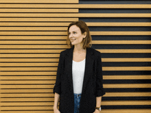 a woman standing in front of a wooden wall wearing a black jacket