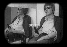 a man is sitting in front of a mirror holding a bottle of beer and the name scott is on the screen