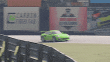 a green car is driving on a race track in front of a sign that says " cartech fiber 643 "