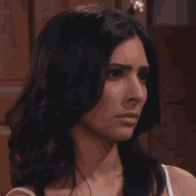 a close up of a woman 's face with dark hair and a white tank top