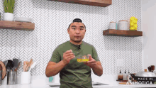 a man in a green shirt is holding a small bowl of oil and a spoon