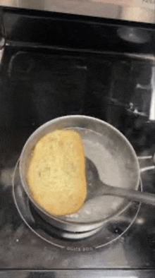 a piece of bread is being scooped out of a pot of boiling water on a stove .