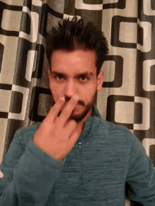 a man with a beard is laying on a checkered blanket and covering his nose with his hand