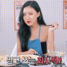 a woman in a blue apron is sitting at a table eating food .