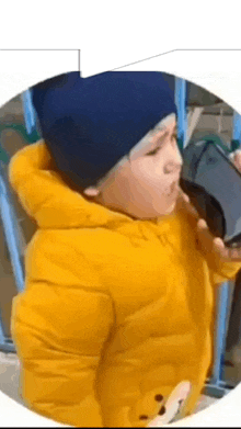 a young boy in a yellow jacket and blue hat is holding a cell phone .