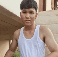 a young man wearing a white tank top is looking at the camera