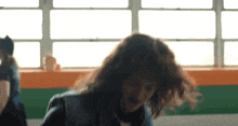a woman with long curly hair stands in front of a window