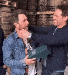 a man in a denim jacket is hugging another man while holding a box that says oei