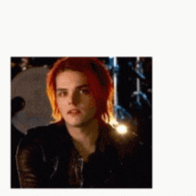 a young man with red hair is wearing a black leather jacket and looking at the camera .
