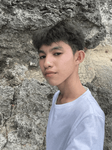 a young man in a white shirt stands in front of a rocky wall