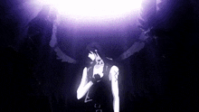 a person with wings is standing in a dark room with a purple light behind him .