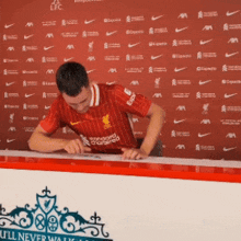 a man in a red liverpool jersey is signing a paper